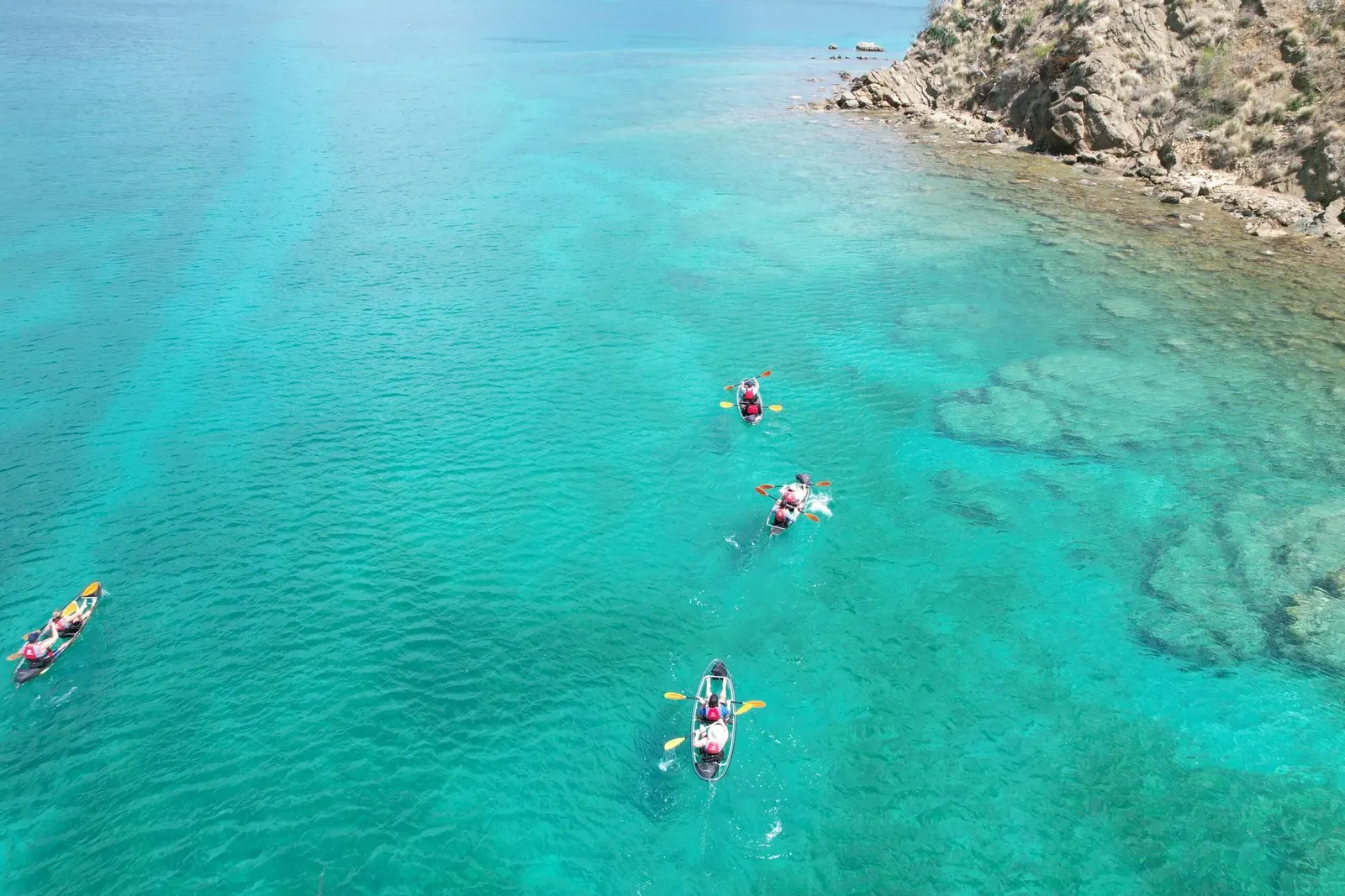 Aerial view of clear kayaks drifting over turquoise water beside the cliffs
