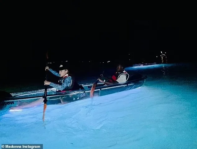 Madonna paddling the illuminated clear kayak across the dark bay