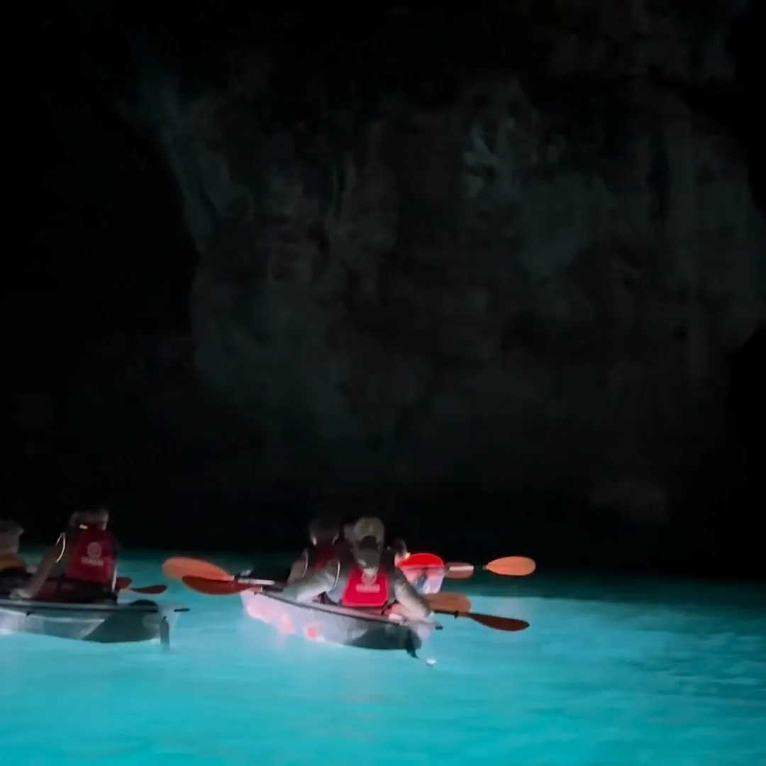 Illuminated clear kayaks glowing turquoise inside the sea cave