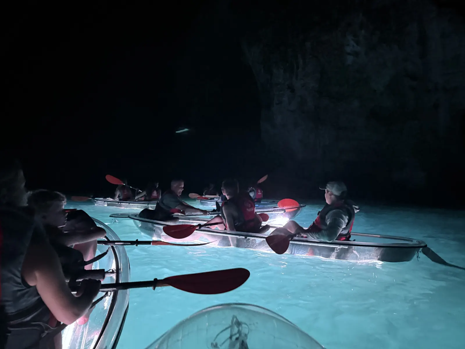 Night tour group in illuminated clear kayaks beneath the cliffs