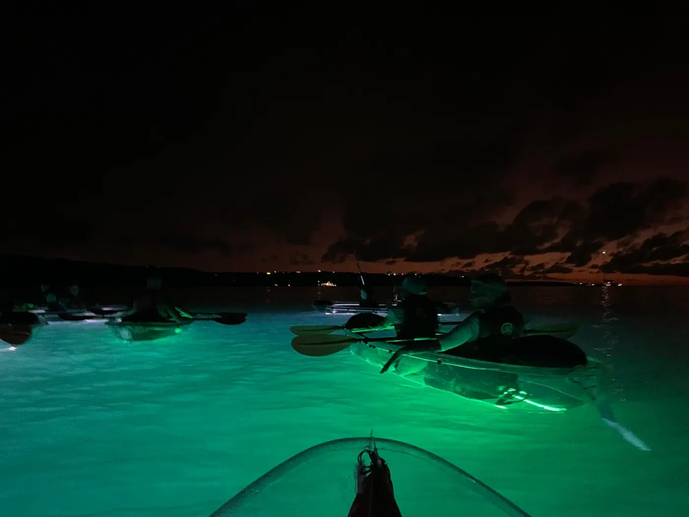 A group of lit clear kayaks turning the bay emerald after dark