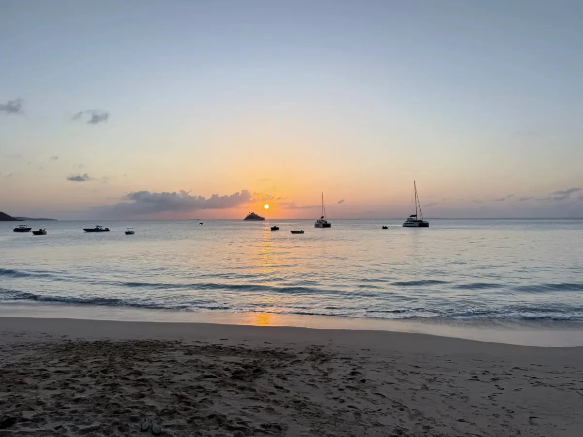 Flip-flops on the sand as the sun sets behind the anchored boats