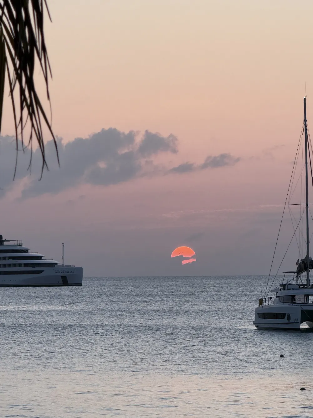 The sun dropping into the sea between a yacht and a catamaran