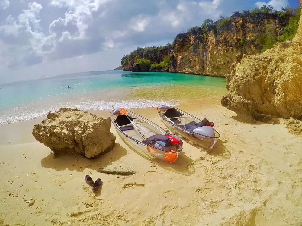 Two clear kayaks resting on the sand at Little Bay beneath the cliffs